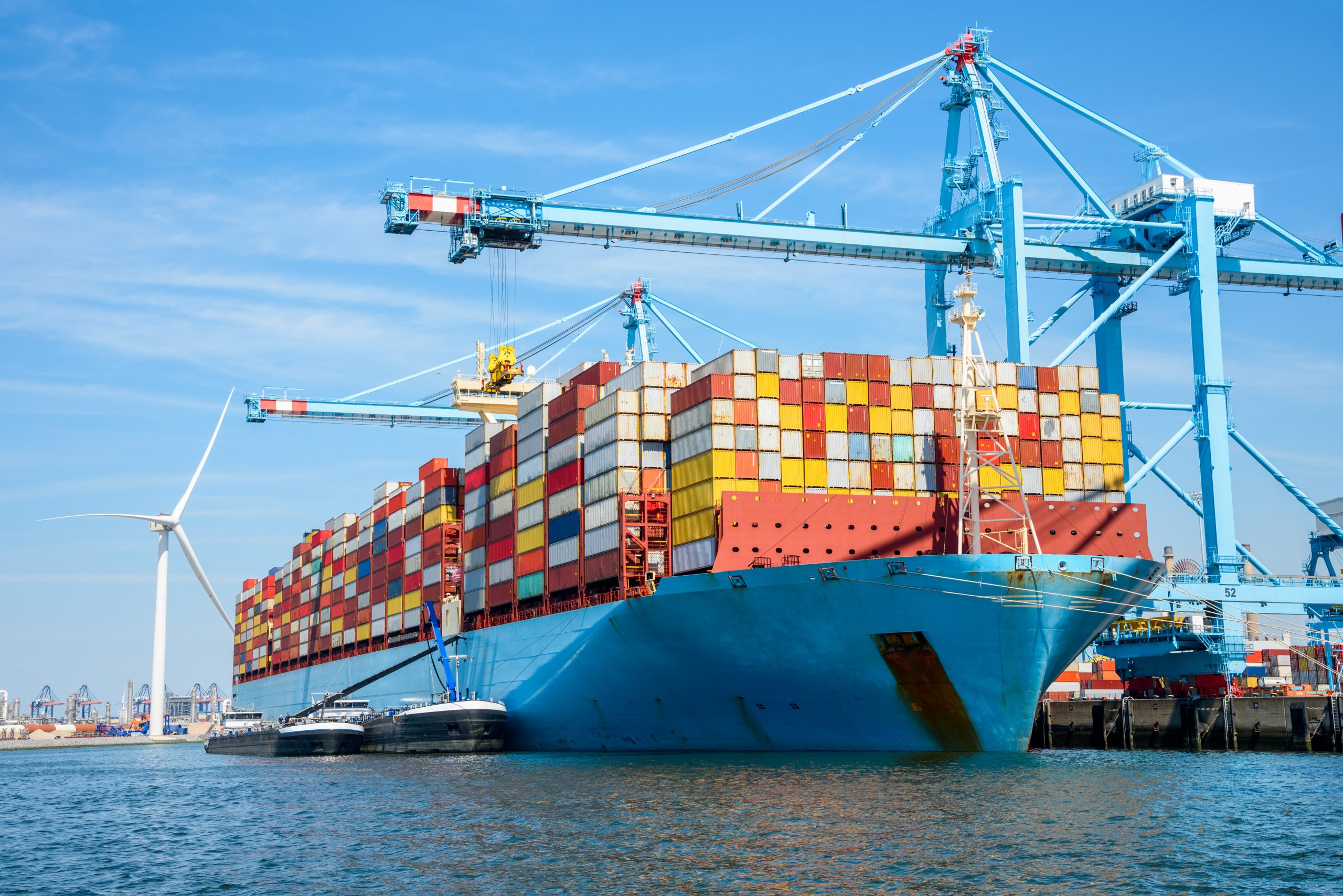 Large cargo ship full loaded with containers docked to a container terminal on a sunny summer day